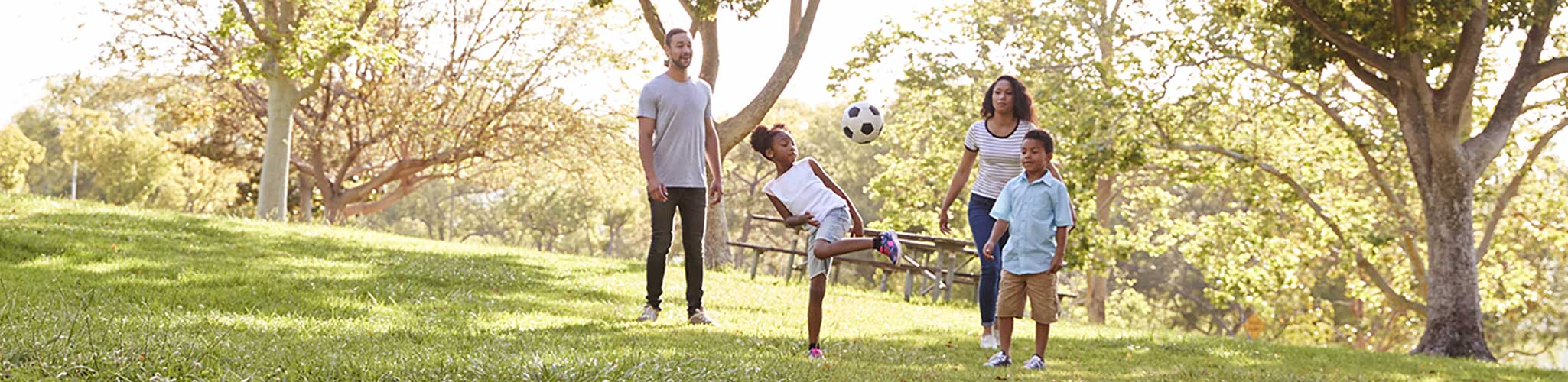 Young family playing soccer in a park.